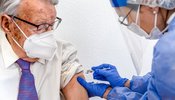 elderly_man_in_mask_watches_as_nurse_in_protective_suit_and_covid_mask_gives_him_coronavirus_vaccine