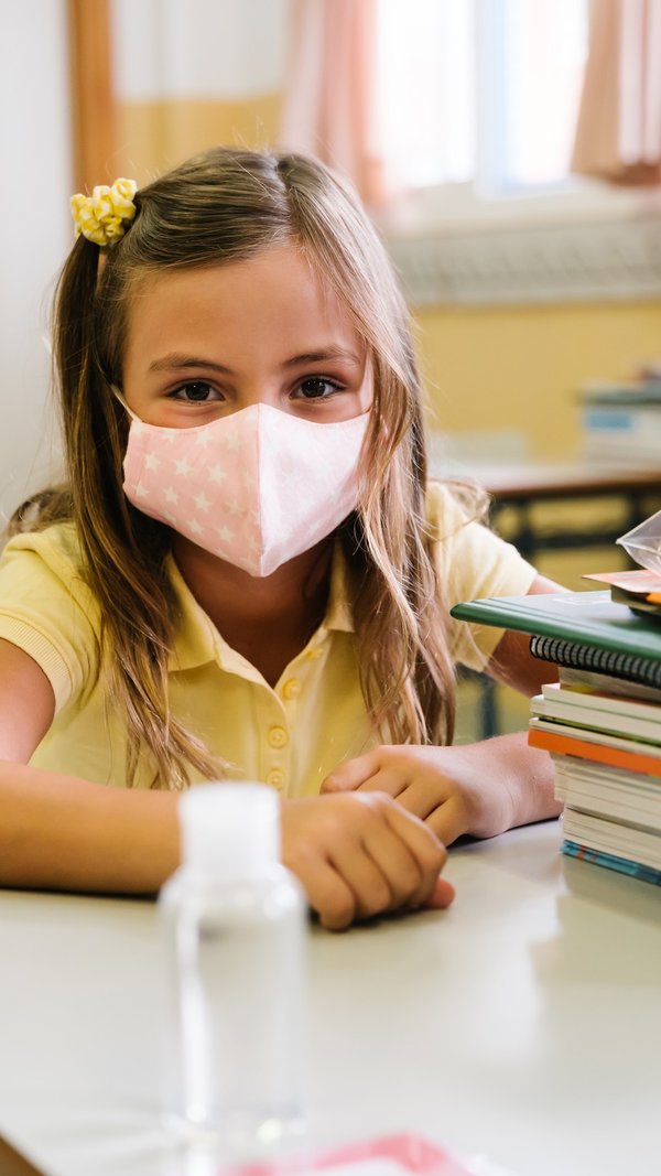 girl_sitting_at_her_chair_and_table_in_the_classroom_wearing_a_mask_to_protect_herself_during_the...